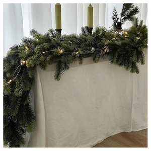 Close-up of realistic pine garland with warm LED fairy lights on a white festive tabletop