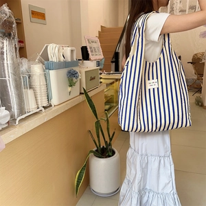 Detailed side view of blue and yellow striped seersucker tote bag in a cozy cafe