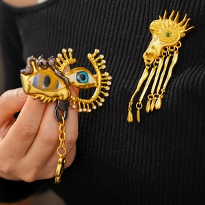Detail of surrealist eye brooches with gold metal fringe and dripping enamel accents