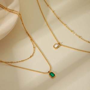 Detail of 18k gold double-layer necklace featuring emerald and clear zircon pendants