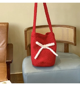 Close-up of red plush bucket bag featuring a white faux fur bow on a light blue stool