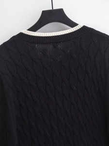 Detail of a black knit cardigan showing cream white collar and twisted cable pattern