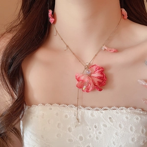 Detail showing delicate pink fabric flower petals and crystal charms on a gold chain necklace