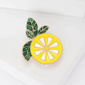 Vibrant enamel lemon slice brooch with green leaves on minimalist white geometric display