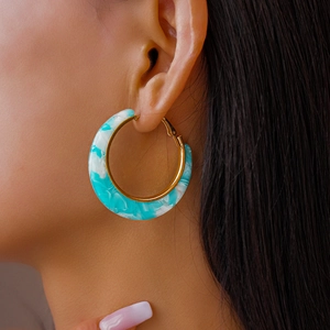 Close-up of blue and white acetate C-hoop earrings with gold-tone metal trim