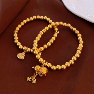 Detail of matte gold beaded bracelets with Buddha head and hollow gourd coin charms