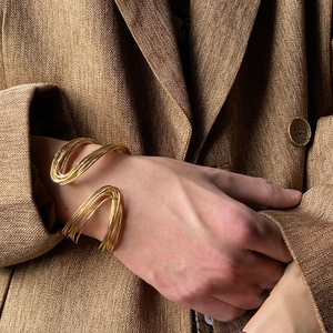 Close-up of a layered gold twisted cuff bracelet on a herringbone blazer sleeve