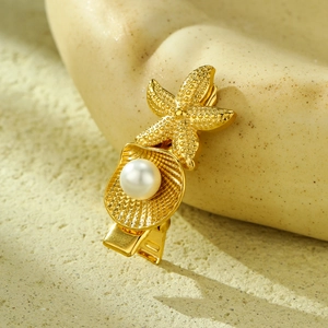Haarklammer in Gold mit Seestern und Muschel mit Perle auf hellem Steinuntergrund