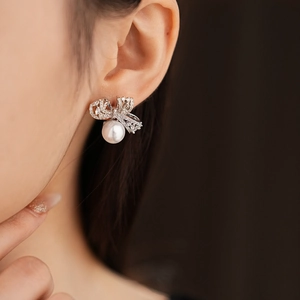Gros plan de boucles d'oreilles nœud en argent avec zircons et perles blanches pendantes