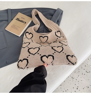 Détail du sac cabas en tricot beige avec motifs de cœurs noirs sur texture de tissu tissé