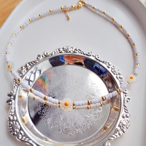 Detail of handmade white heishi bead daisy necklace with golden accents on a vintage plate