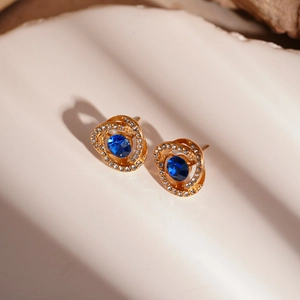 Close-up of golden floral earrings with blue gemstone and micro-pave diamond accents