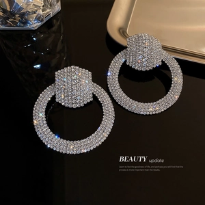 Exaggerated silver circle drop earrings with full rhinestones on a black background