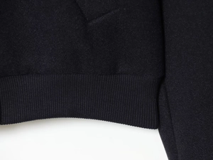 Gros plan sur les poignets et l'ourlet en maille côtelée noire du manteau en laine