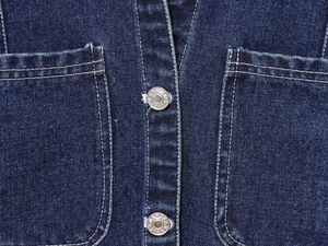 Détail de la veste en jean bleu foncé avec boutons métalliques et surpiqûres blanches