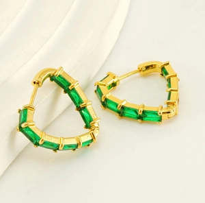 Detail of heart-shaped gold earrings with emerald green rectangular cut zircon stones