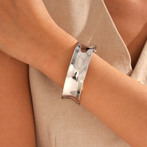 Close-up of wide polished silver metal cuff bracelet worn on wrist with glossy finish