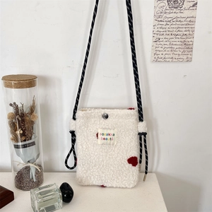 Close-up of white plush crossbody bag featuring a red 3D heart and woven shoulder strap