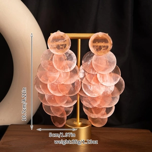 Detail view of pink seashell layered earrings with size dimensions on a display stand