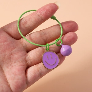 Close-up of green wire bracelet with purple smiley face charm and matching bell pendant