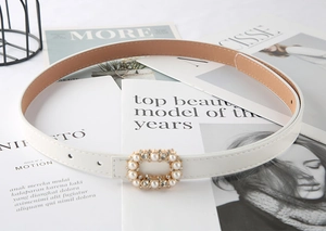 Close-up of a white leather belt for women featuring a pearl and rhinestone buckle design