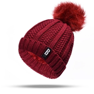 Detail of burgundy knit beanie with metallic shimmer, faux fur pom-pom, and B-logo patch
