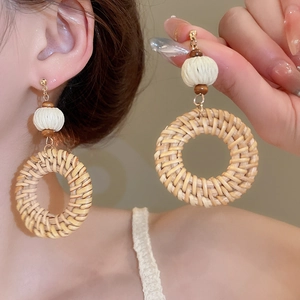 Detail of bohemian rattan woven hoop earrings with white knit balls and wooden beads