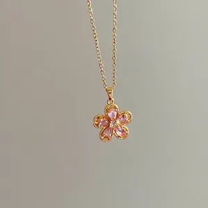 Elegant gold flower necklace with pink crystal petals and central zircon on grey background