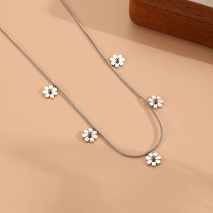 Détail du collier en chaîne argentée avec cinq pendentifs fleurs délicats sur fond beige