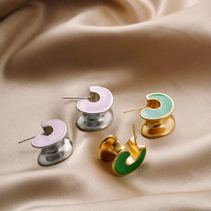 Detailed macro view of C-shaped enamel earrings in pink and green on silk fabric