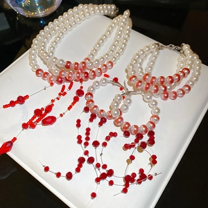 Detailed view of elegant multi-layer pearl jewelry set with red crystal tassels on white tray