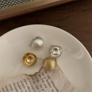 Close-up of matte silver and gold spherical earrings on a vintage paper background