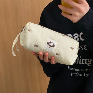 Detail of cream quilted makeup bag featuring brown bow embroidery and cartoon character