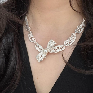Vue détaillée du collier pendentif nœud en dentelle argentée avec une perle blanche