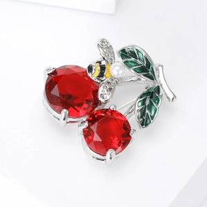 Close-up of crystal cherry brooch with red gemstones, green leaves and a small bee