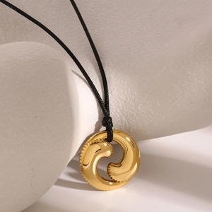 Nahaufnahme des goldenen hohlen Anhängers an schwarzer Schnur auf weißer Geometrie