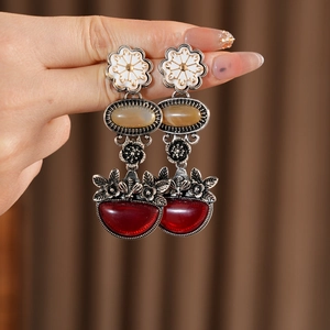 Macro detail of vintage floral drop earrings featuring white enamel and red resin elements