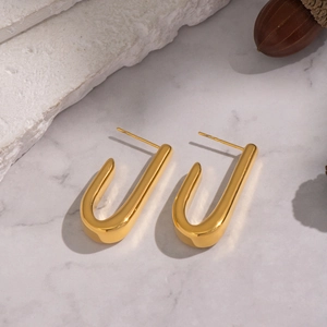 Detail of minimalist 18K gold plated fishhook earrings on a marble surface backdrop