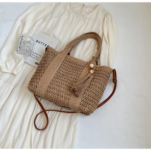 Flat lay of khaki straw tote bag with woven texture, tassel charm, and shoulder strap