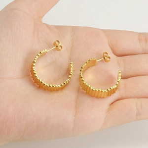 Détail des boucles d'oreilles créoles C en acier doré avec textures verticales