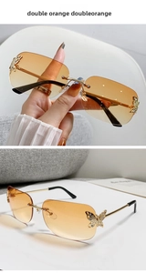 Detail of rimless rectangle sunglasses with metal butterfly accents and orange lenses