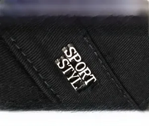 Detailed close-up of the metal SPORTS STYLE logo plaque on a black twill flat top cap
