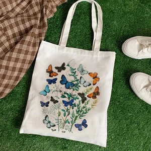 White canvas tote bag with vintage butterfly and floral prints on green grass background