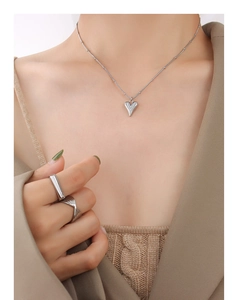 Detail of silver heart pendant necklace and textured rings on elegant model outfit