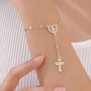 Détail d'un bracelet doré avec charm cœur scintillant et petit pendentif croix