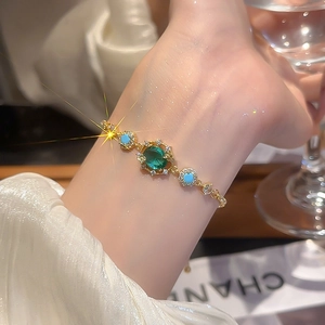 Detailed shot of an 18k gold plated bracelet with green and blue oval zircons on wrist