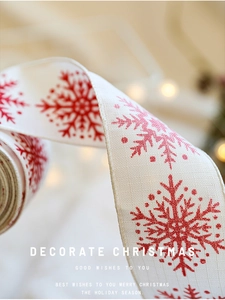 Detail of cream faux linen Christmas ribbon with red snowflake prints and soft bokeh light