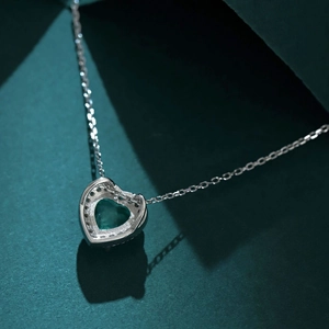 Macro shot of a heart-shaped green gemstone necklace with shadow on textured background