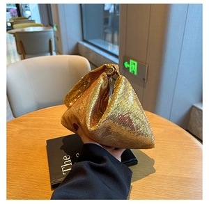Détail d'un sac à main doré à paillettes avec structure triangulaire tenu en main