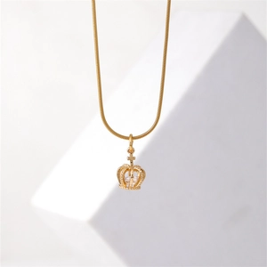 Elegant gold crown pendant necklace with snake chain and crystal detail on a white pedestal